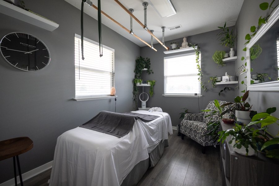 The Ashi Studio at CGW Studios: Ashiatsu bars on the ceiling, plant-filled walls, comfortable seating, and natural light streaming in.